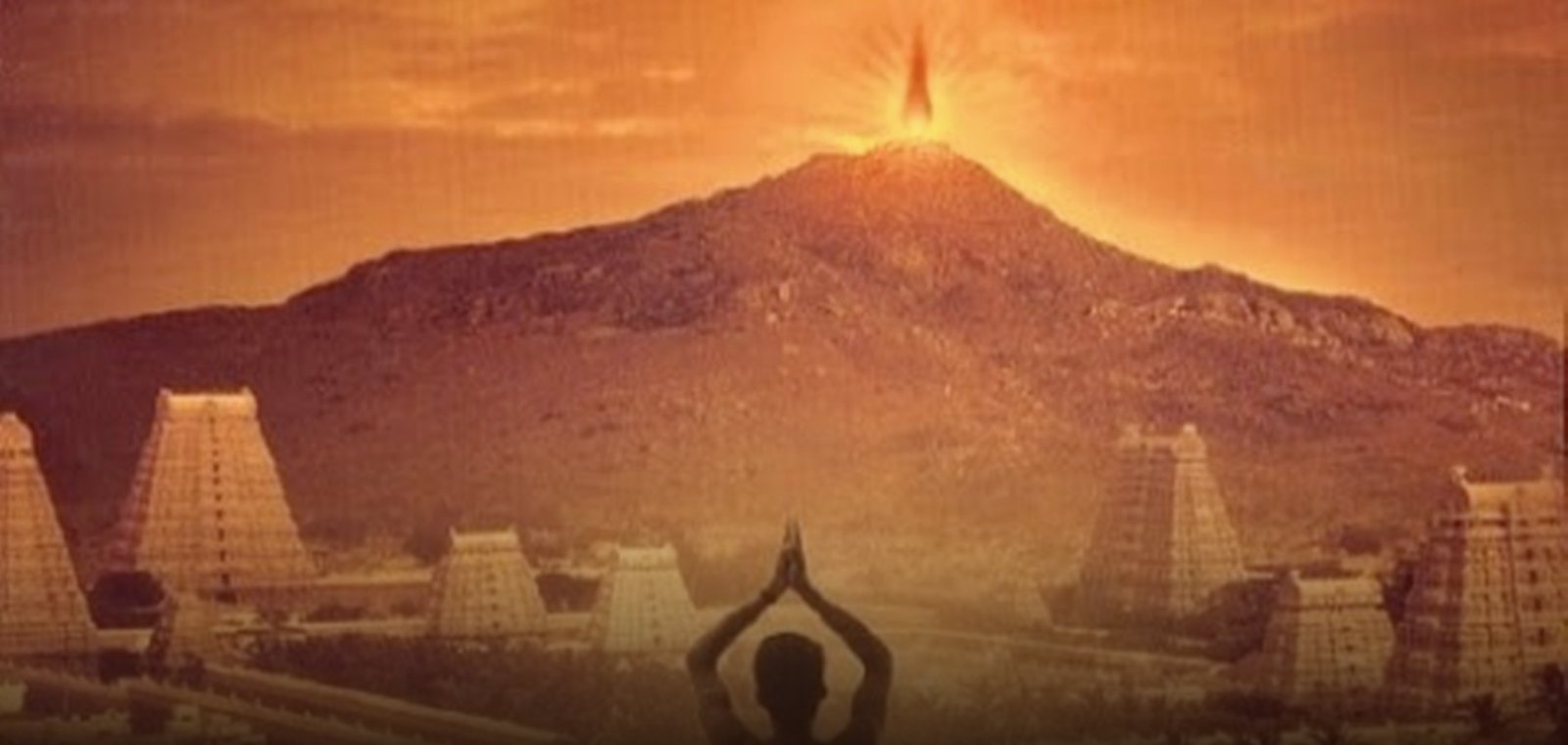 The Maha Deepam flame blazing atop Arunachala hill on Karthigai Deepam, with the temple gopurams and a devotee below